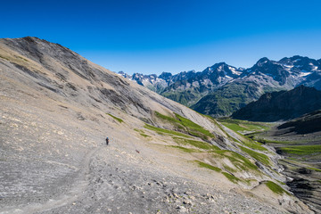 A hiker slowly ascending the trail toward the Vallonpierre Pass in the Ecrins National Park, French Alps