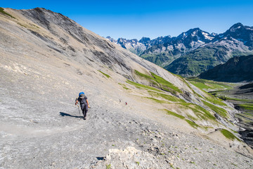 A hiker slowly ascending the trail toward the Vallonpierre Pass in the Ecrins National Park, French Alps