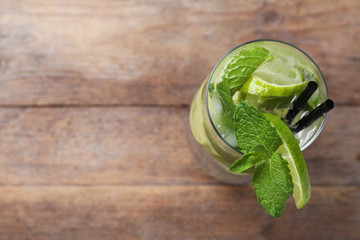 Glass of tasty refreshing cocktail with lime and mint on wooden background, above view. Space for text