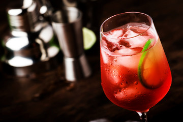 Campari tonic alcoholic cocktail with red bitter, tonic, lime and ice. Old wooden table background, bar tools, selective focus. All names refer to cocktails, not trademarks