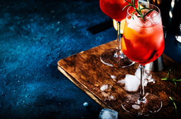 Milano spritzer alcoholic cocktail with red bitter, dry white wine, soda, zest and ice. Dark blue background, bar tools, selective focus