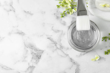 Professional face mask with brush and flowers on white marble table, flat lay. Space for text