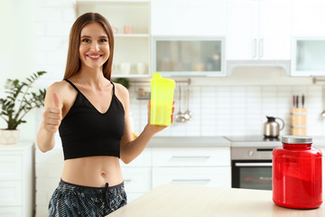 Fototapeta na wymiar Young woman with bottle of protein shake in kitchen