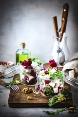 Beet and cheese healthy salad with arugula and walnuts, trendy salad jar, gray kitchen table, place for text, selective focus