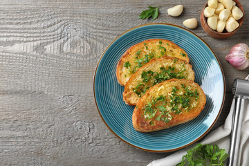 Slices of toasted bread with garlic and herb on wooden table, flat lay. Space for text