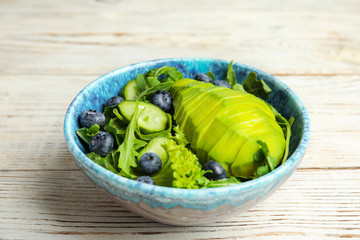 Delicious avocado salad with blueberries in bowl on white wooden table