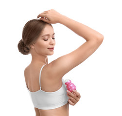 Young woman applying deodorant to armpit on white background