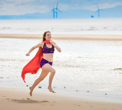 beautiful girl playing on beach with a superhero cape