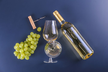 Unopened vintage bottle of white wine without label and bunches of ripe organic grapes on matte blue table background. Expensive bottle of chardonnay concept. Copy space, top view, flat lay.