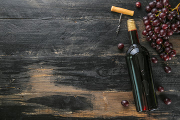 Vintage bottle of red wine without label, corkscrew & bunches of ripe organic grapes on grunged...