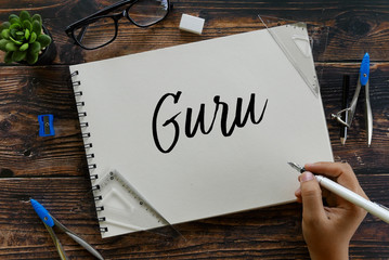Top view of stationery with hand writing Guru on notebook on wooden background.