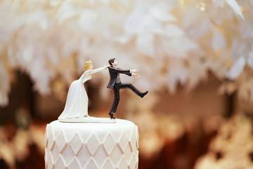 groom doll and statue is running away but bride can catch him finally. the funny wedding story doll on the top of cake.