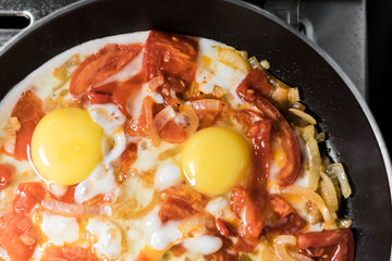 Fried eggs with onions, tomato and pepper, cooking in a pan, breakfast, healthy lifestyle