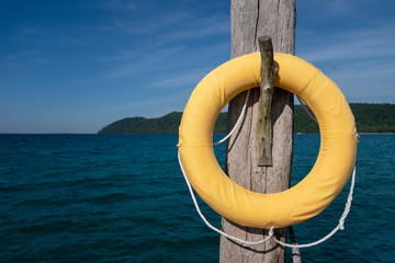 luxury classic Safety Torus covered by yellow cloth. It hangs on to old wooden pole settle on the jetty in the sea.