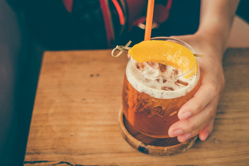 The glass of peach ice tea on wooden table in coffee shop.iced tea cocktail, cold drink or lemonade with fruits.Vintage tone.