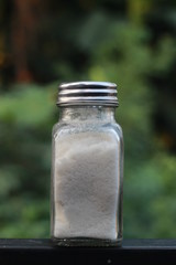 salt from small shaker at garden, green background