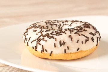 Fresh glazed donut with chocolate sprinkles on a white plate.
