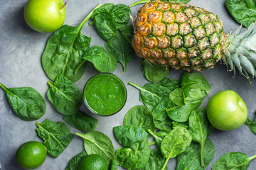 Glass with green raw smoothie with ingredients vegetables spinach fruits pineapple citrus apples on...