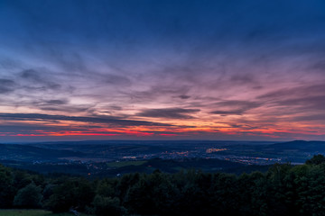 The setting sunset over the town of Valasske Mezirici as the city and its surroundings public light up slowly multi colored dark clouds and sun hiding below horizon.