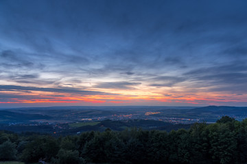Obraz premium The setting sunset over the town of Valasske Mezirici as the city and its surroundings public light up slowly multi colored dark clouds and sun hiding below horizon.
