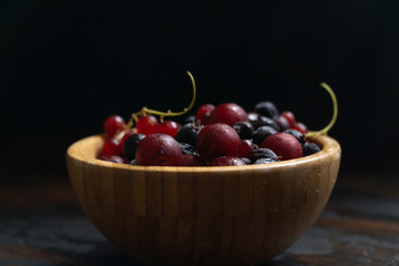Ripe black and red currants in a wooden bowl on a wooden table. Organic food, harvest season.