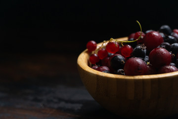 Ripe black and red currants in a wooden bowl on a wooden table. Organic food, harvest season.