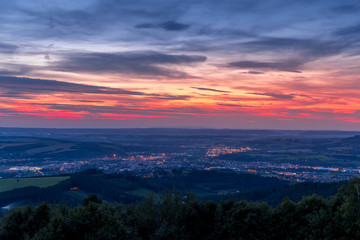 The setting sunset over the town of Valasske Mezirici as the city and its surroundings public light up slowly multi colored dark clouds and sun hiding below horizon.