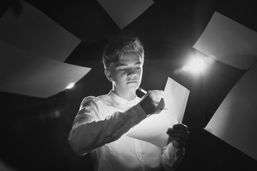 Expressive teenager in a white shirt with a piece of paper and a pen in the throes of creativity, a...