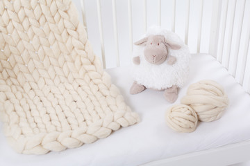 Plaid Merino wool hand-knitted, lying on a child's bed. Near the balls of wool and white sheep.