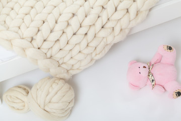 Plaid Merino wool hand-knitted, lying on a child's bed. Near the balls of wool and a pink Teddy bear.