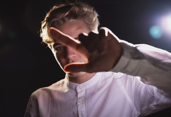 Expressive teenager in a white shirt in bright light, emotional young man with strong hands and beautiful eyes