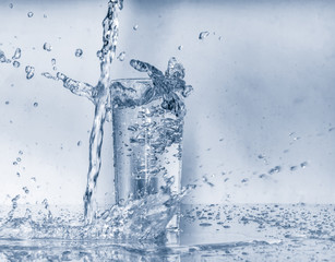 Water splashes and pouring water into glass on blue background