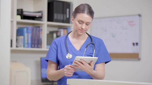 Nurse with stethoscope reviews a patient file on tablet, subtle move left right.