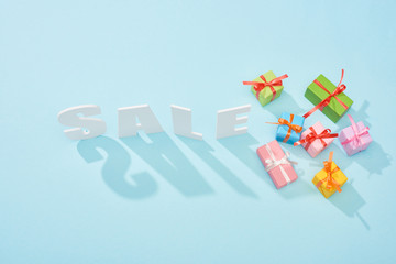 top view of white sale lettering with shadow and festive gift boxes on blue background