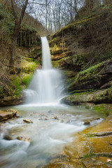Sunlit, colorful forest waterfall streaming down the red rocks in it's amphitheater during spring 