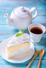 Coconut cake decorated with coconut meat and mint leaf on a white plate, With a tea of ready-to-drink and a teapot placed on a wooden floor. To feel the atmosphere in the morning.
