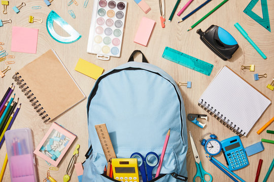 Top view of various school supplies with blue backpack on wooden desk