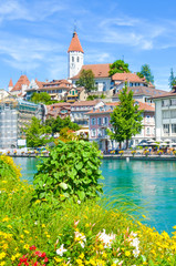 Naklejka premium Bed of flowers by Aare river in Switzerland. The historical center of Swiss city Thun in the background, partly blurred. Dominant of the city is famous castle. Beautiful Swiss cities. Vertical photo