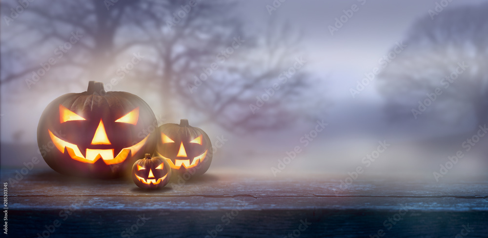 Wall mural a ghostly dusk in the countryside with spooky jack o' lanterns in the fog with bare trees in the bac