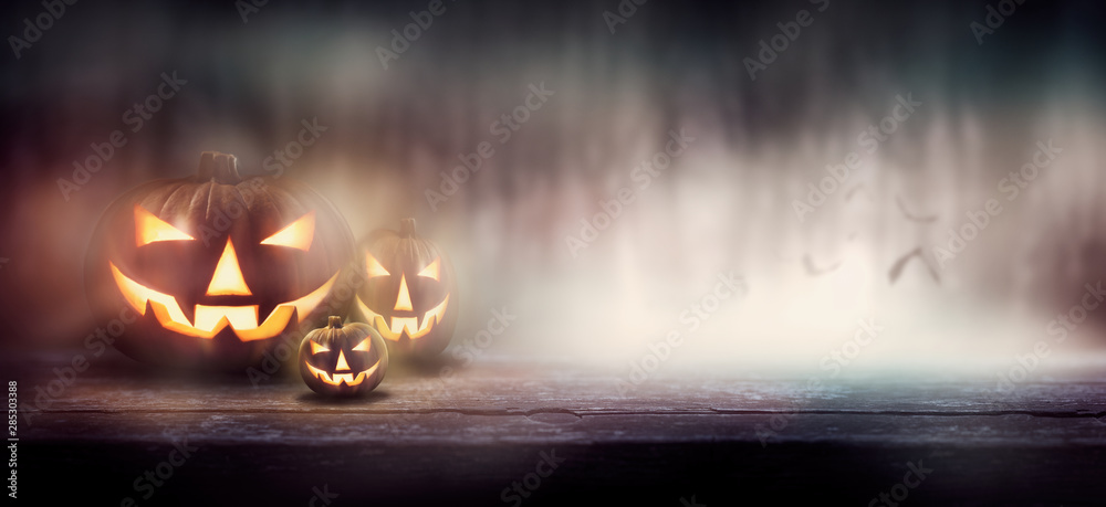 Wall mural the evil glowing eyes of jack o' lanterns through mist and fog in a forest on a halloween night.