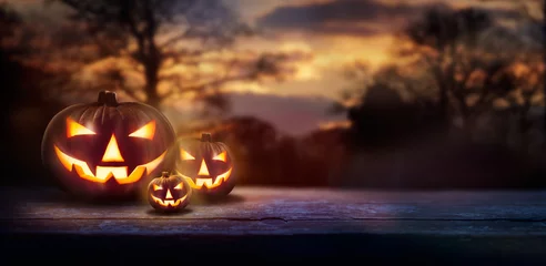 Gordijnen Een spookachtige boszonsondergang met achtervolgd kwaad gloeiende ogen van Jack O& 39  Lanterns aan de linkerkant van een houten bank op een enge Halloween-nacht. © Duncan Andison