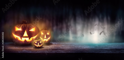 Warm glow of Jack O' Lanterns on a wood bench in a dark cold forest at night.