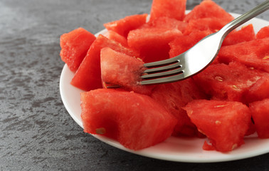 Plate of watermelon chunks with a fork on a gray mottled table side view