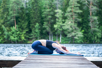 Young attractive girl practicing yoga, sitting in Child exercise, Balasana pose  on the lake. The concept of appeasement,  healthy lifestyle