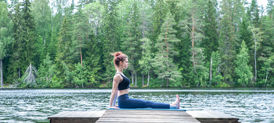 Young yogi  girl  practicing yoga, sitting in Staff exercise, Dandasana pose on the lake. The concept of appeasement,  healthy lifestyle.  Panoramic view