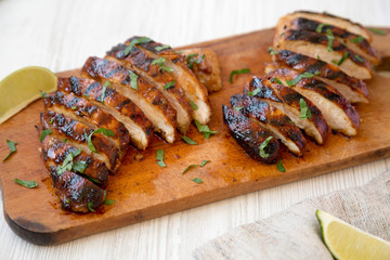 Grilled chipotle chicken breast on a rustic wooden board on a white wooden surface, side view. Close-up.