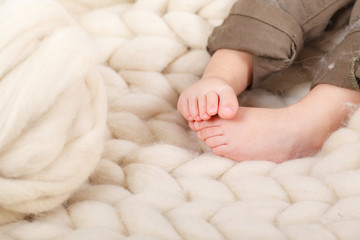 A small baby sitting on a blanket of merino wool. Plaid on boards.