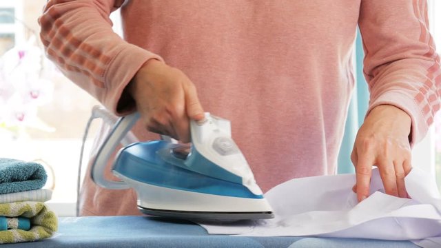 Female hands ironing clothes with iron on ironing board