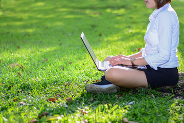 Young woman using computer on green grasses in the park. freelance working outdoor or relaxation concept.
