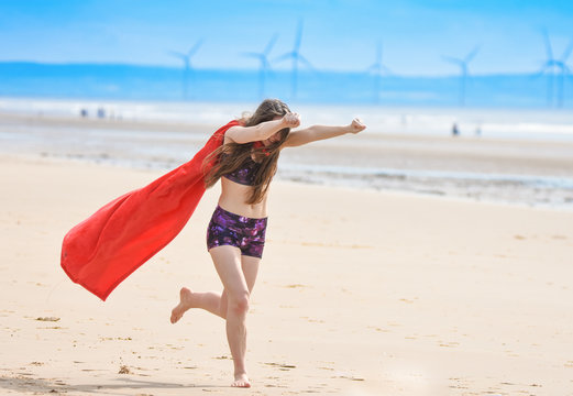 beautiful girl playing on beach with a superhero cape